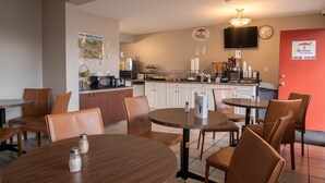 A breakfast area with tables and chairs, a kitchen in the background, and a clock on the wall. - Super 8 by Wyndham Kamloops East (Kamloops)