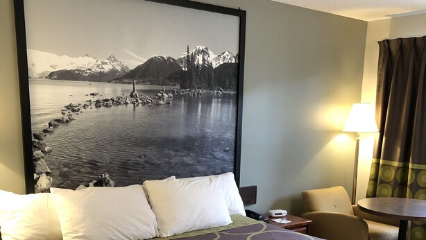 A hotel room with a large bed, a nightstand, a lamp, and a view of a mountainous landscape. - Super 8 by Wyndham Kamloops East (Kamloops)