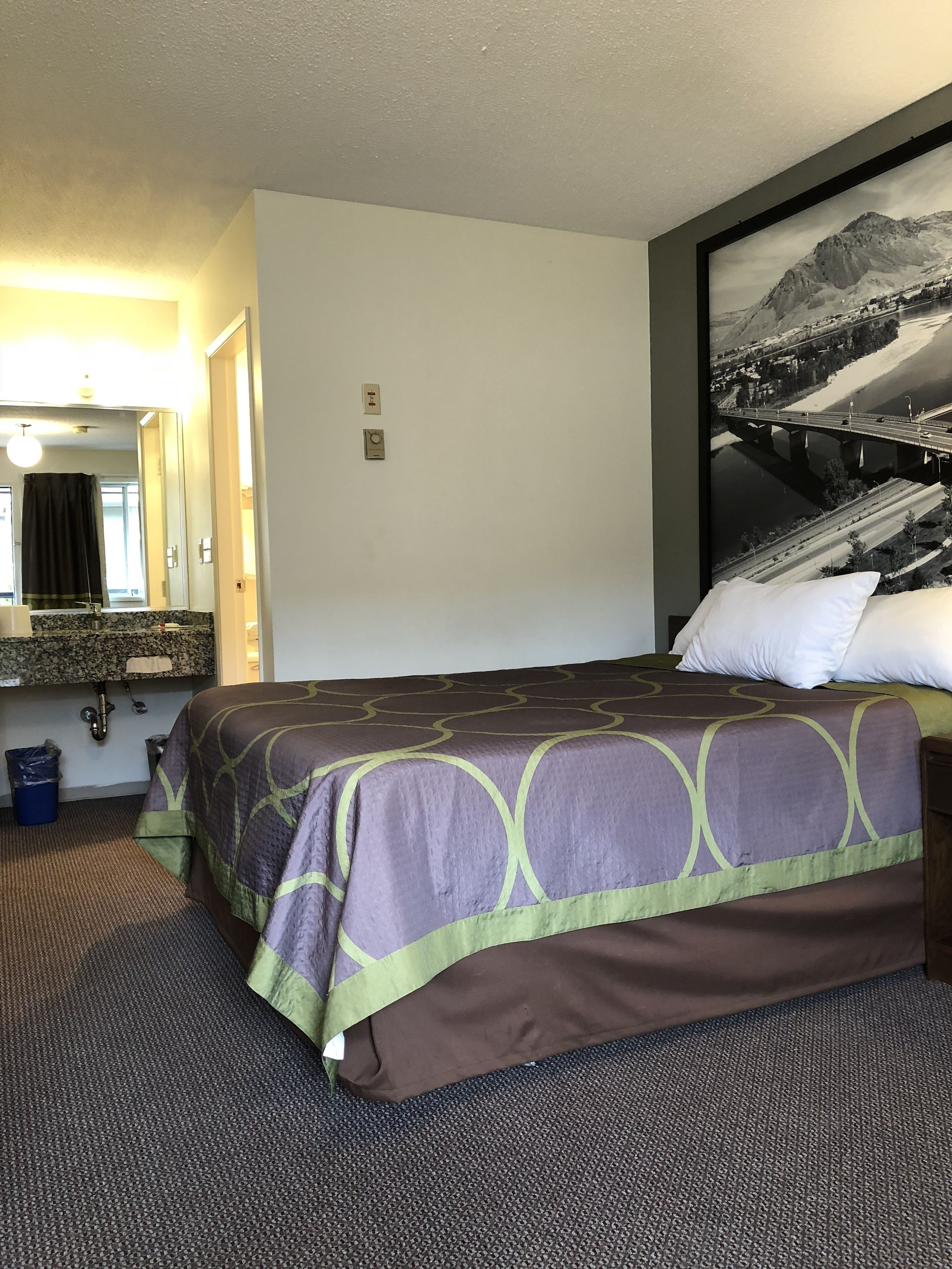 A hotel room with a bed, a large mirror, a bathroom, and a framed picture on the wall.