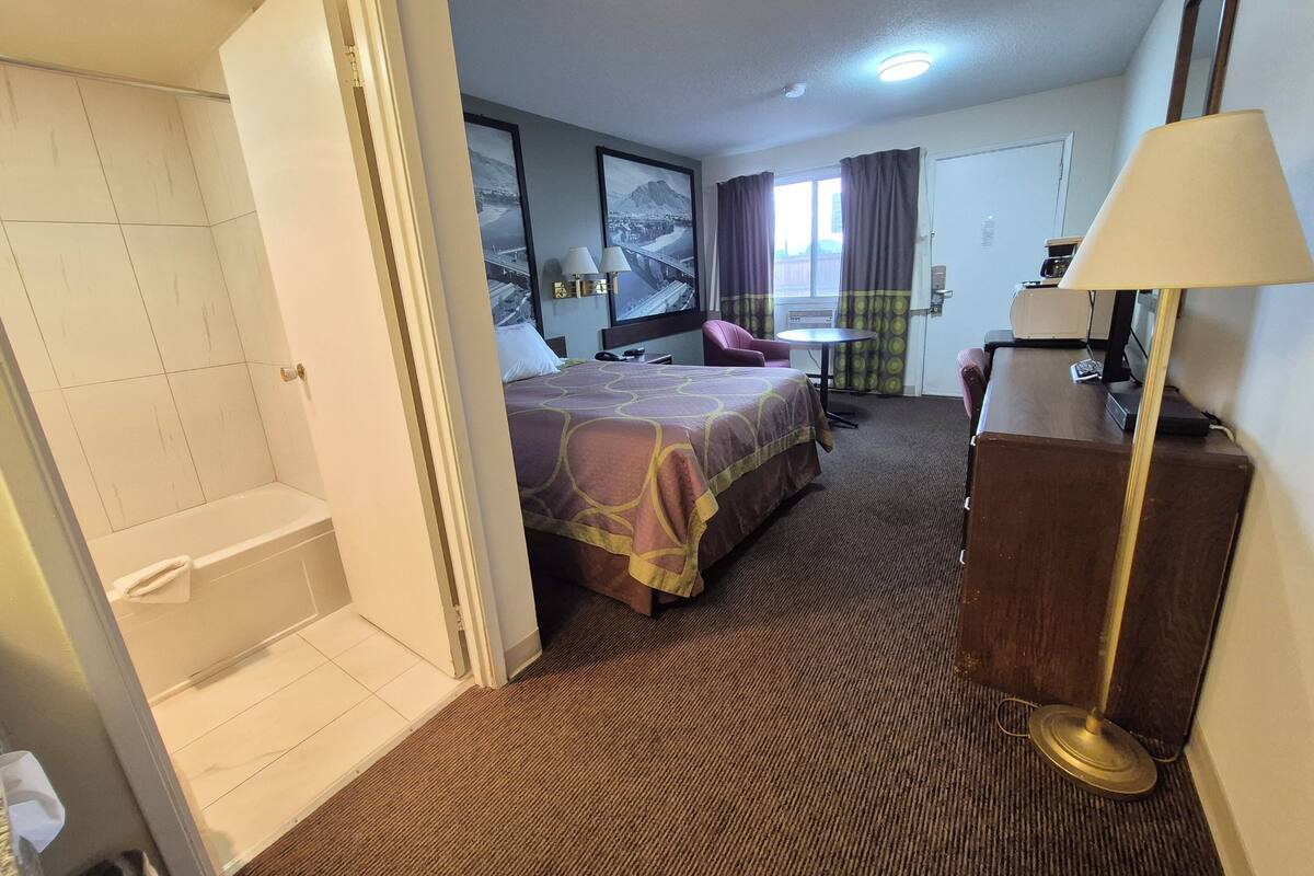 Une chambre d’hôtel comprenant un lit, un bureau, une chaise, une lampe, une salle de bain et une vue sur l’extérieur.