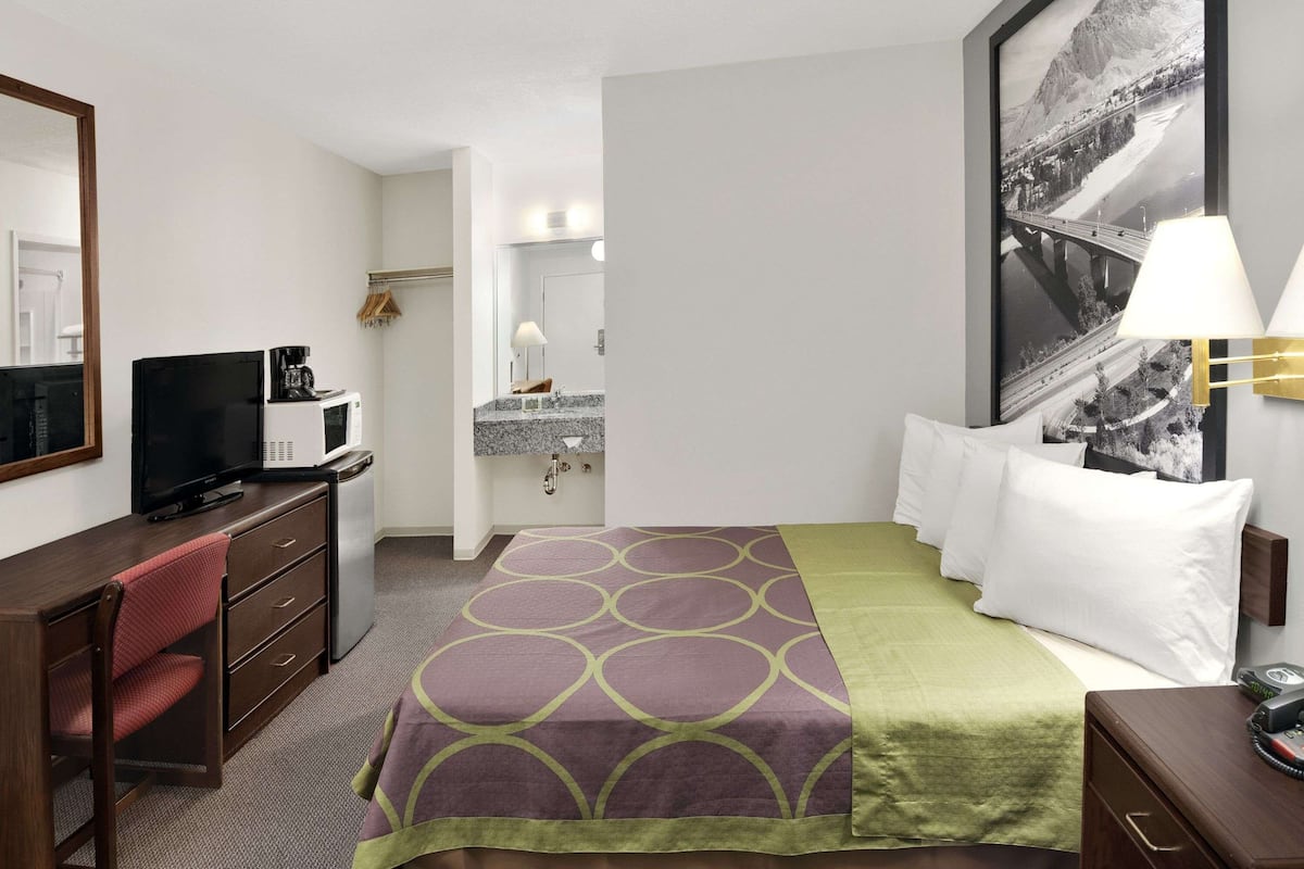 Une chambre d’hôtel avec un lit, un bureau doté d’une télévision, un four à micro-ondes et une salle de bain visible à travers une porte ouverte.