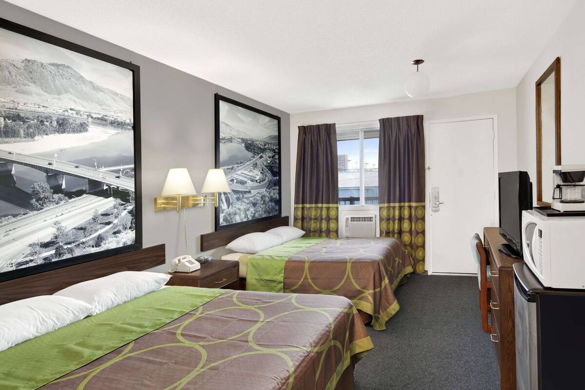 Une chambre d’hôtel avec deux lits, un bureau, un four à micro-ondes et une grande fenêtre avec des rideaux.