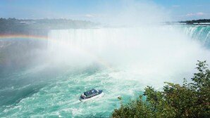 Un bote navegando una cascada con un arcoíris al fondo.