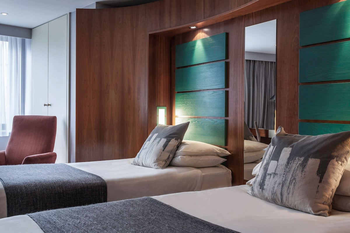 A hotel room with two beds, a red armchair, and a wooden partition with green panels.