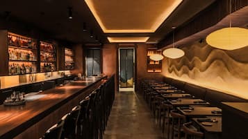 A bar with a long counter, multiple seating areas, and a patterned wall.
