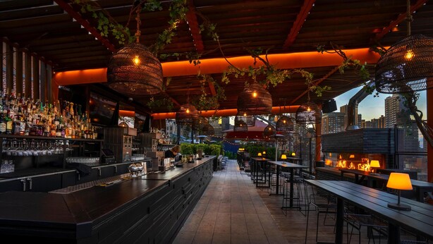 A bar area with a long counter, hanging wicker lamps, and a city view in the background. - Park South Hotel, part of JdV by Hyatt (New York)