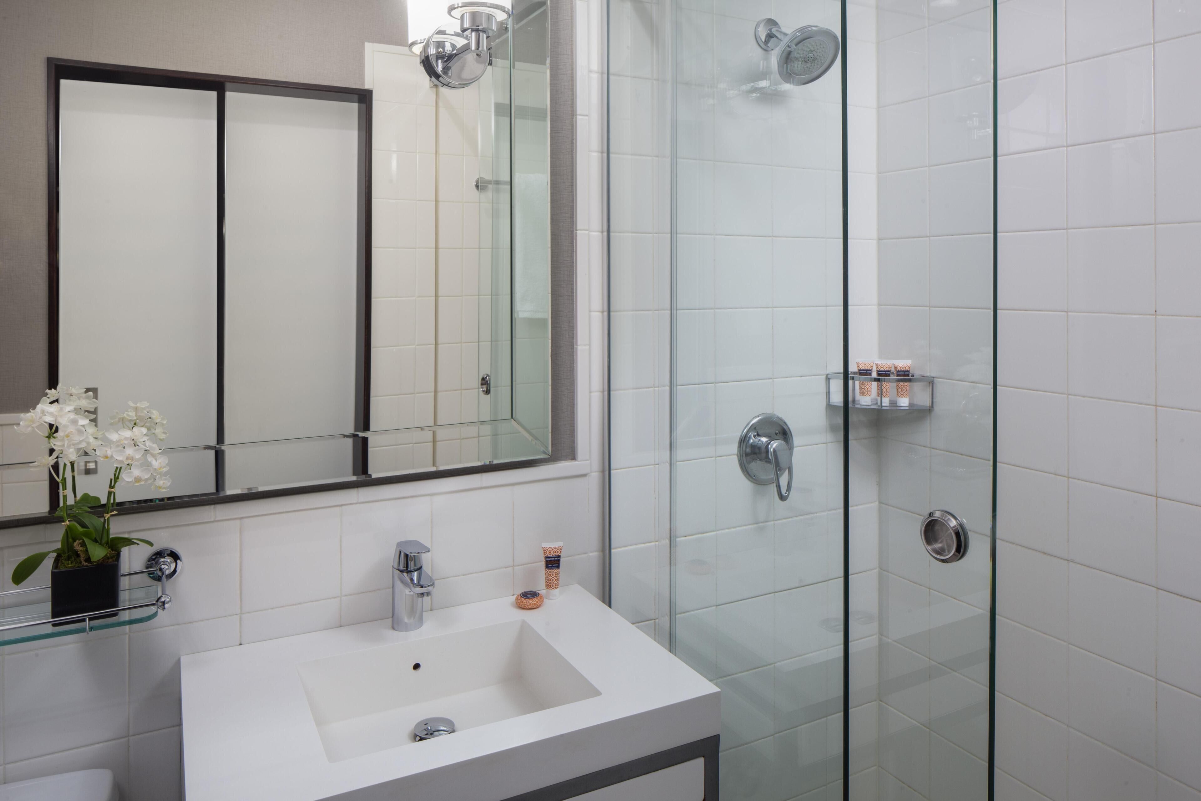 A bathroom with a glass shower enclosure, a white sink, a mirror, and a potted orchid.