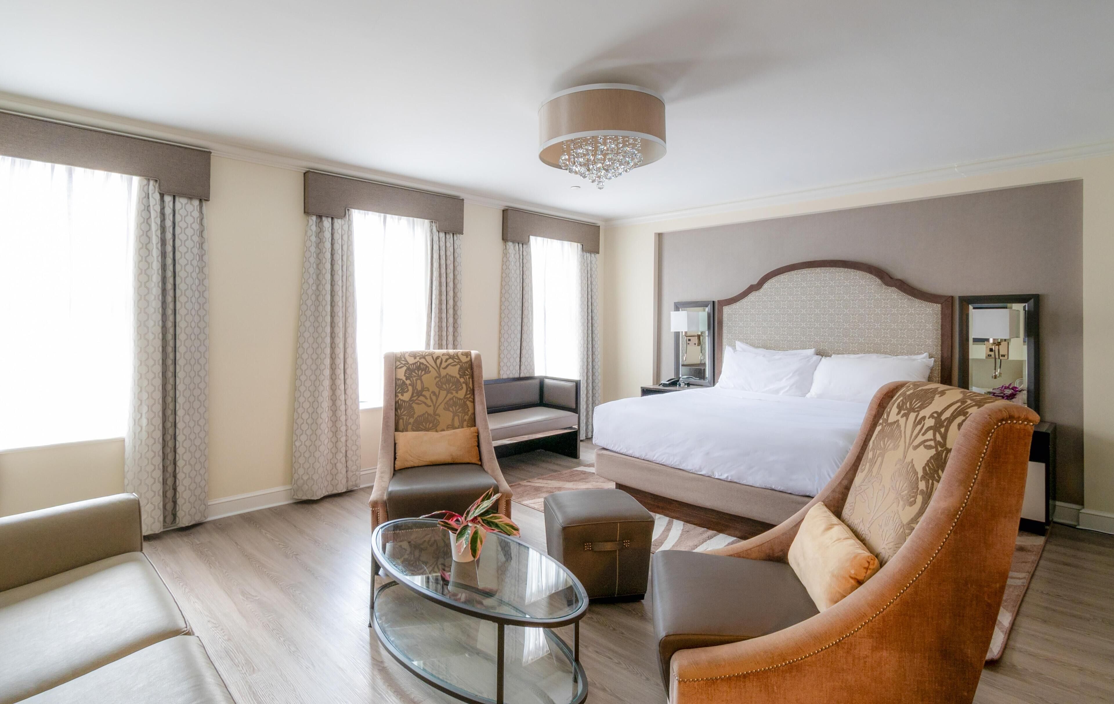 A hotel room with a large bed, a sofa, a chair, a small table, and a chandelier.