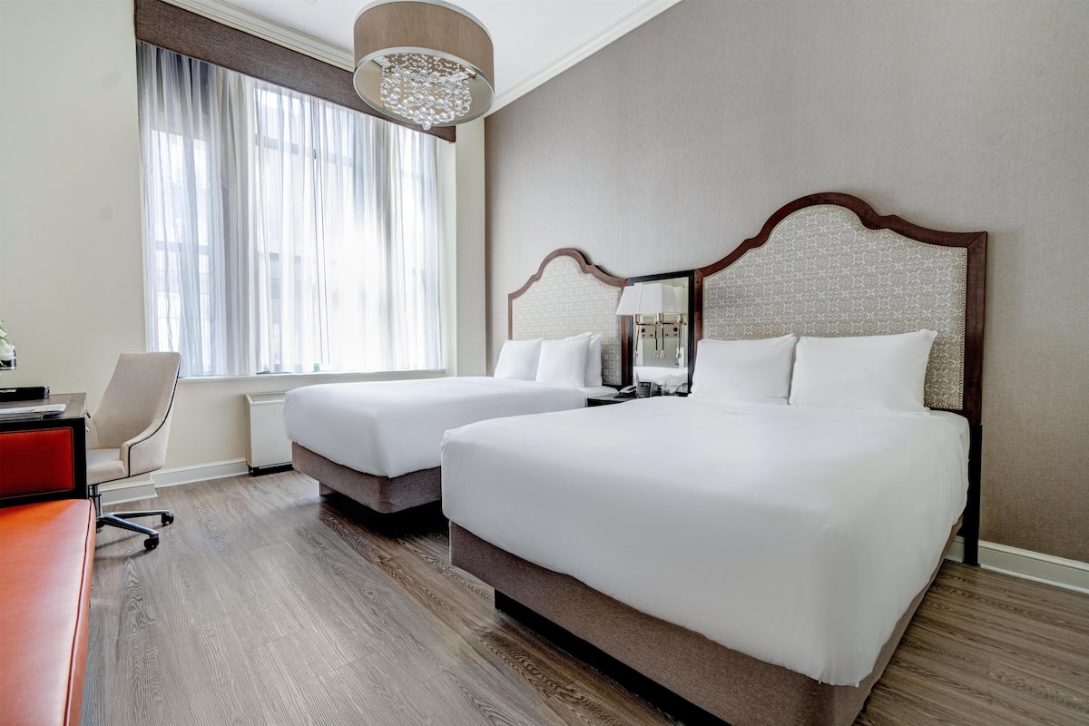 Quarto de hotel com duas camas, uma escrivaninha e uma cadeira.