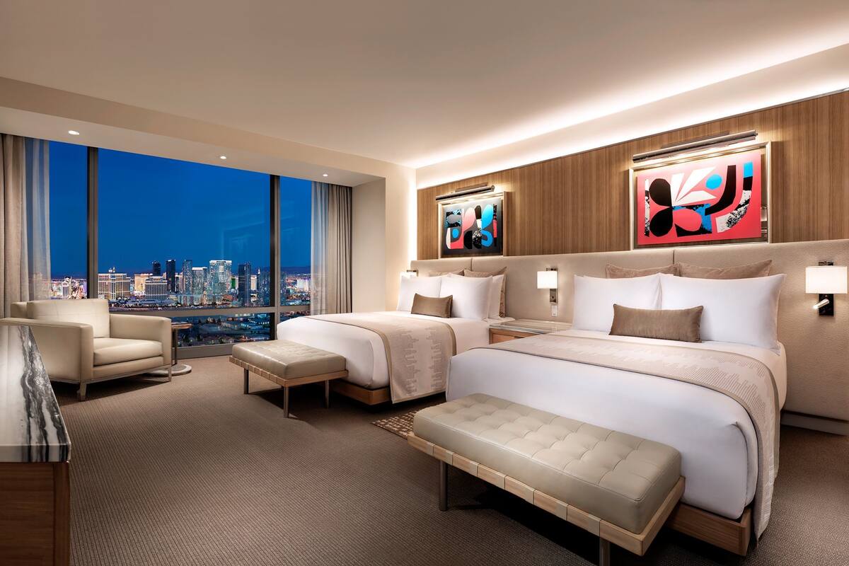 A modern hotel room with a large bed, two bedside tables, a chair, and a view of a cityscape at night.