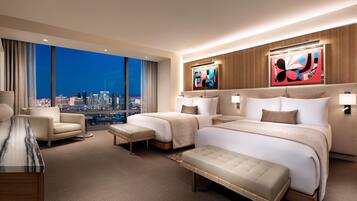A modern hotel room with a large bed, two bedside tables, a chair, and a view of a cityscape at night.