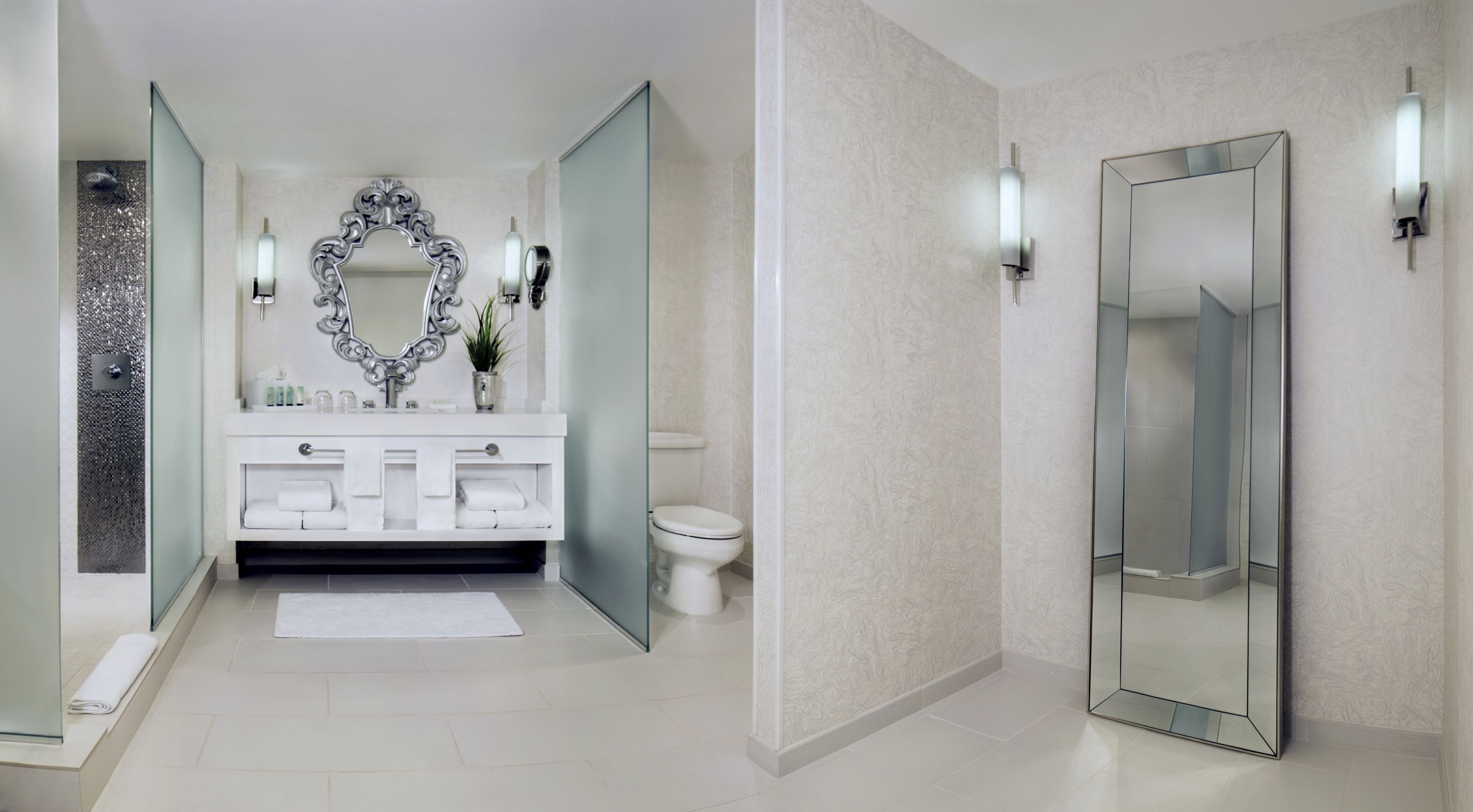A modern bathroom with a large mirror, two sinks, a toilet, and a glass shower enclosure.
