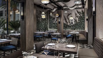 A restaurant with a checkered floor, wooden pillars, and hanging pendant lights. Tables are set with plates and glasses.