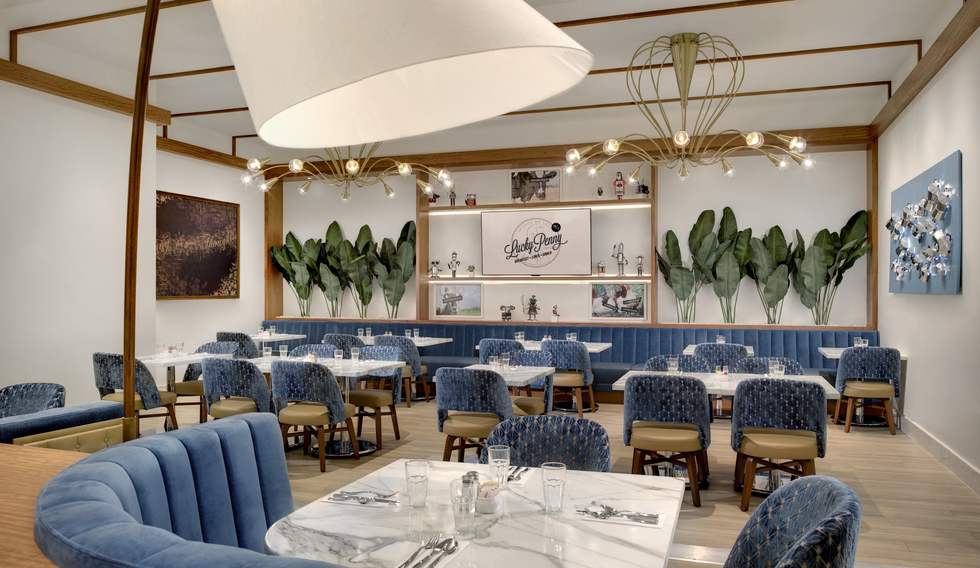 A restaurant with blue upholstered booths and tables, a large chandelier, and wall-mounted artwork.