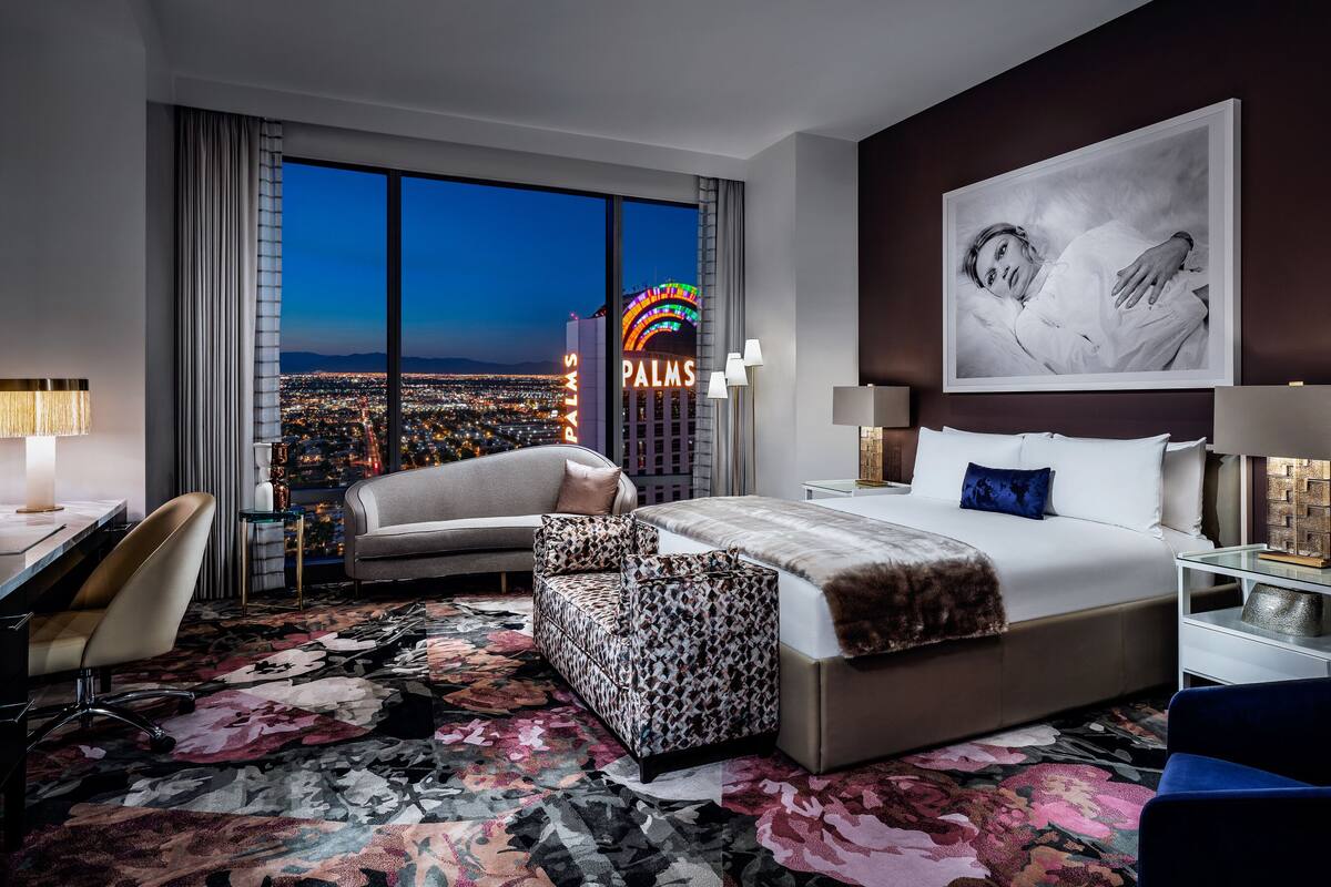 A hotel room with a large bed, a desk, a chair, and a view of the cityscape.