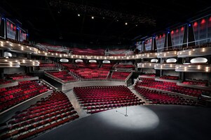 Un ampio teatro moderno con numerosi livelli di posti a sedere e un palcoscenico centrale.