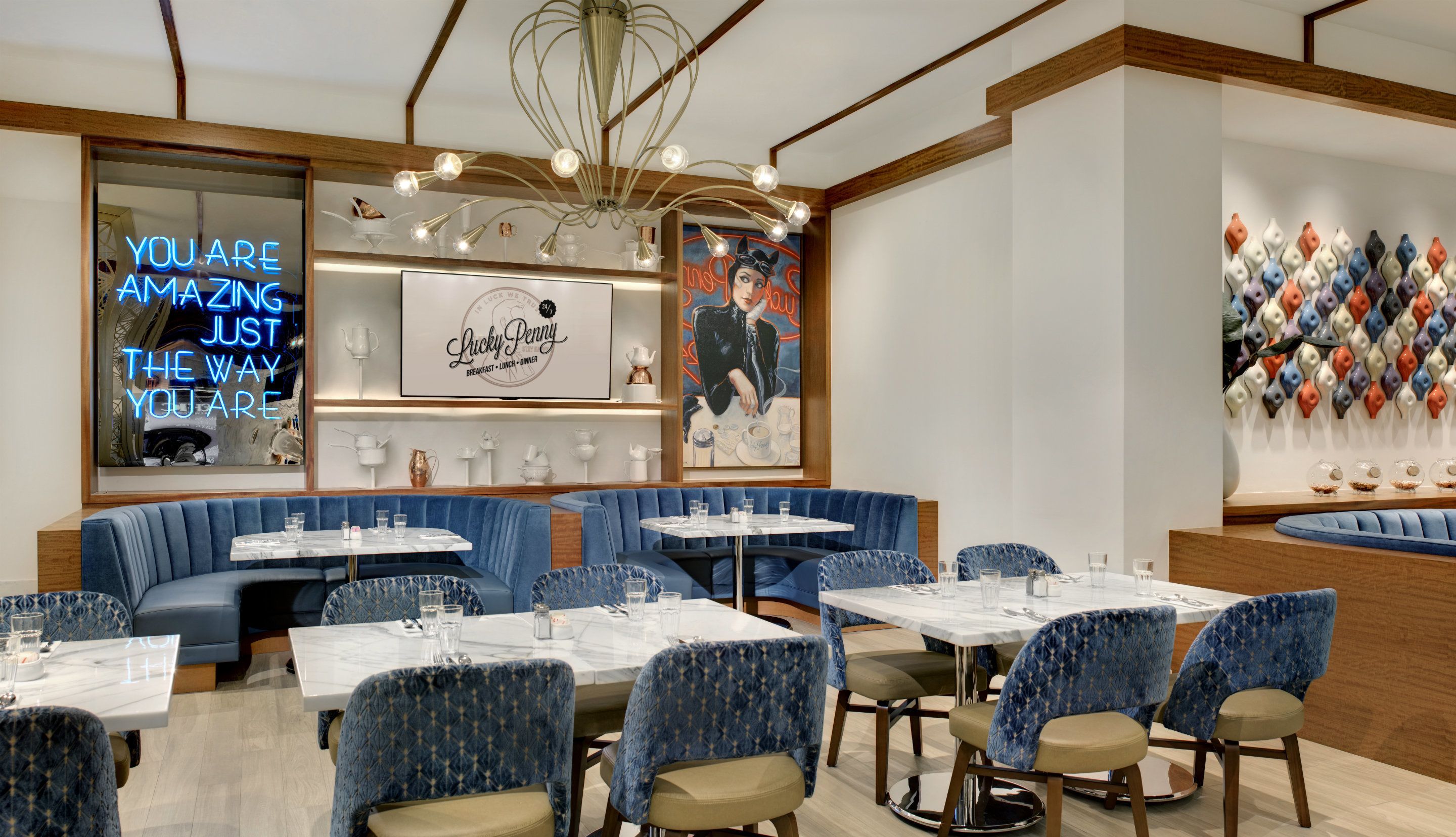 Interior de restaurante con asientos tapizados en azul, mesas de mármol y un letrero de neón.