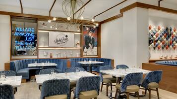 Interior de restaurante con asientos tapizados en azul, mesas de mármol y un letrero de neón.