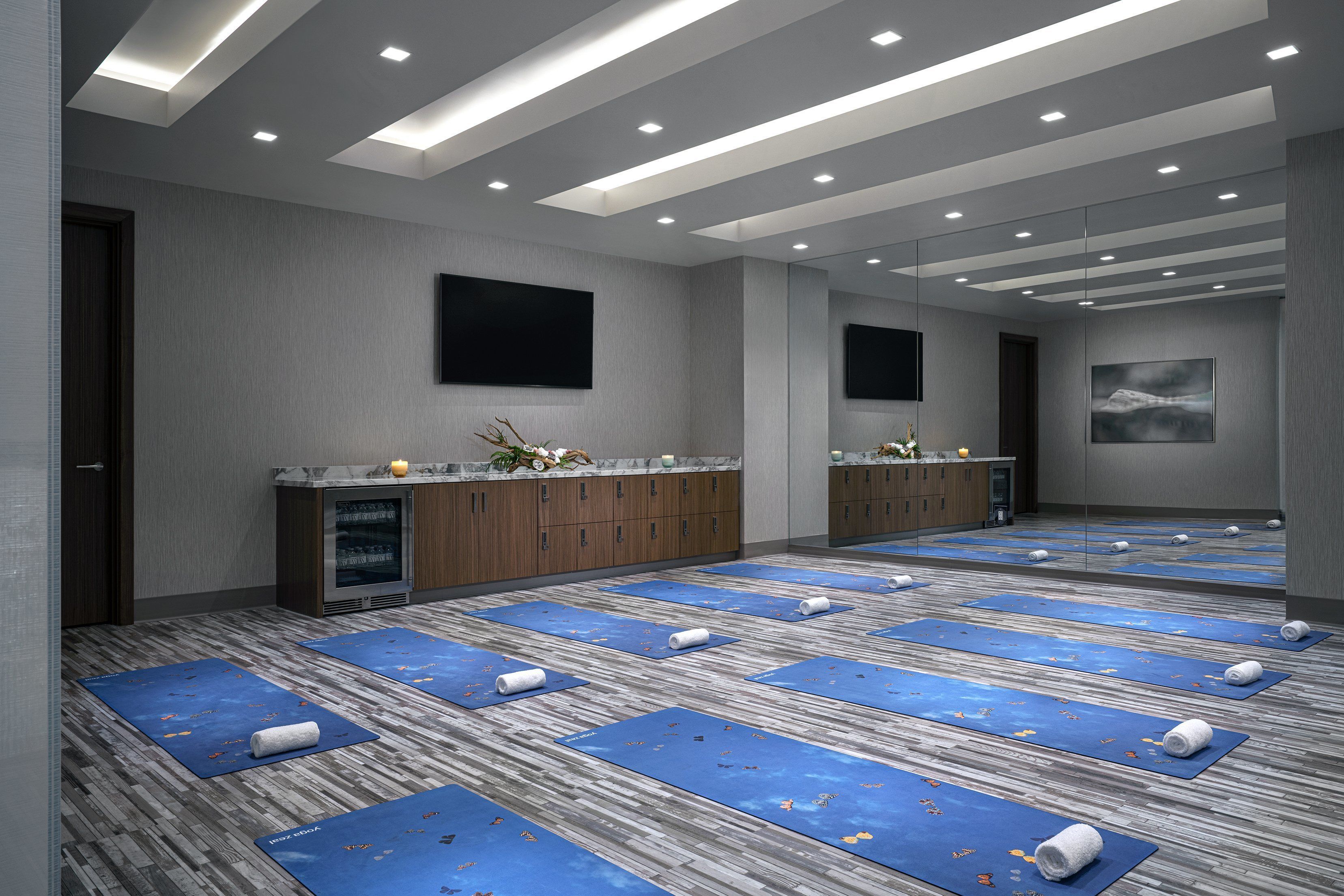 Une chambre d’hôtel moderne dotée d’un grand miroir, d’un téléviseur à écran plat et de plusieurs tapis de yoga disposés sur le sol.