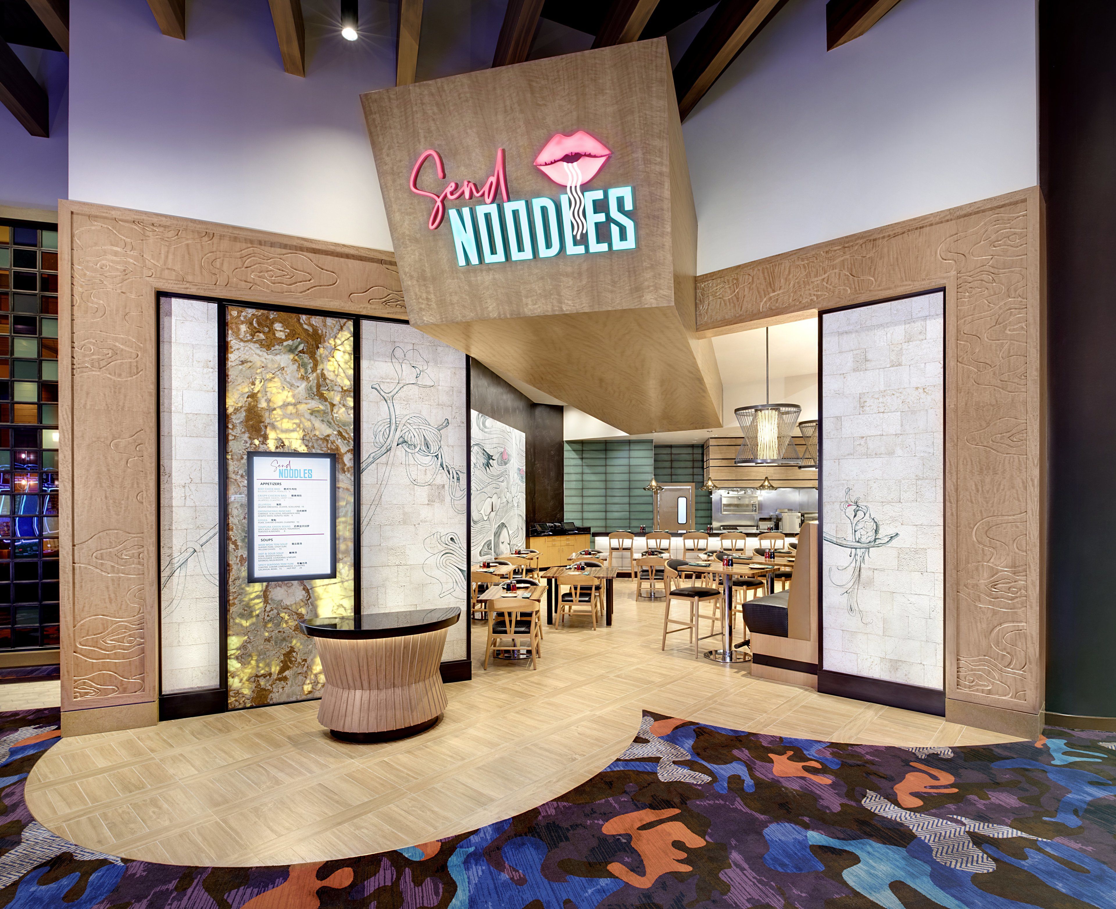 A modern restaurant interior with a prominent 'Send Noodles' sign, wooden paneling, and a central seating area.