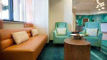Un moderno vestíbulo de hotel con alfombra color turquesa, un sofá de cuero marrón y dos sillones color turquesa con cojines estampados.
