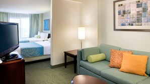 A hotel room with a green sofa, a television on a wooden stand, a small table, and a bed with blue bedding. - SpringHill Suites Los Angeles LAX/Manhattan Beach (Hawthorne)