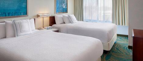A hotel room with two beds, a nightstand, a lamp, and a large window with curtains.