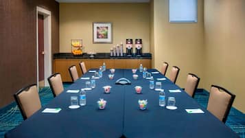 A conference room with a long table, chairs, water bottles, and coffee makers.