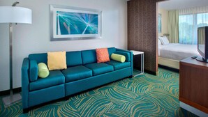 A hotel room with a teal sofa, a framed abstract painting, a television, and a patterned carpet. - Willow Grove Inn (Willow Grove)