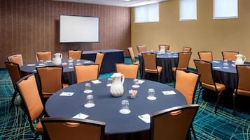 Une salle de conférence équipée de tables rondes, de chaises, d’un écran de projection et d’un sol recouvert de moquette.