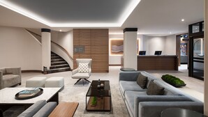 A modern hotel lobby with a reception desk, seating area, staircase, and a kitchen visible in the background. - AC Hotel by Marriott Old Montreal (Montreal)