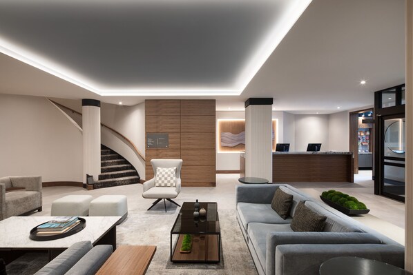 A modern hotel lobby with a reception desk, seating area, staircase, and a kitchen visible in the background. - AC Hotel by Marriott Old Montreal (Montreal)