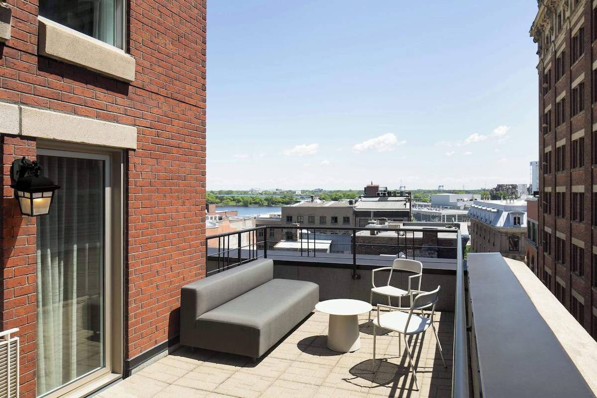 A rooftop terrace with a grey sofa, two white chairs, and a small round table.