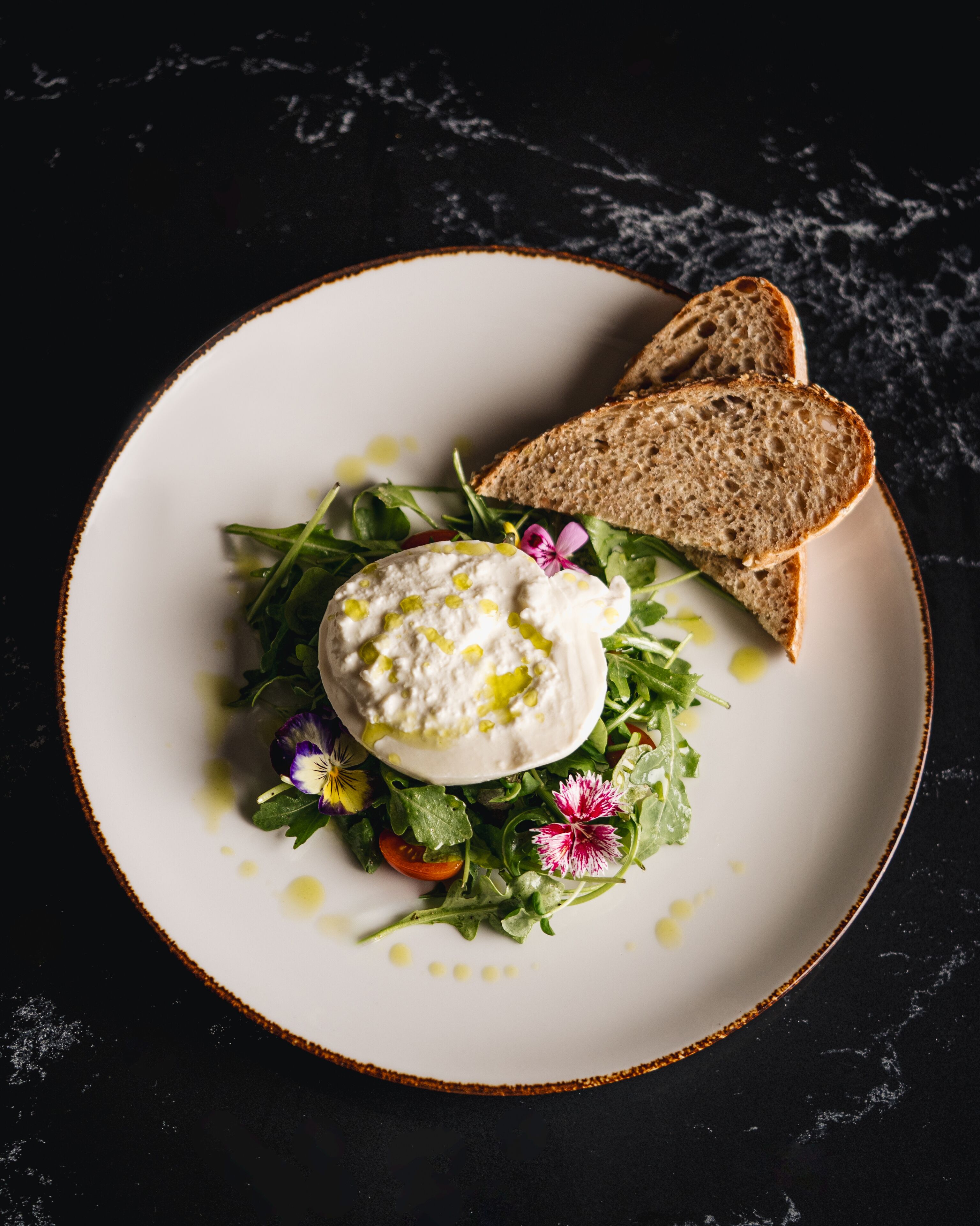 A plate with a white sauce, greens, and two slices of bread on a dark surface.