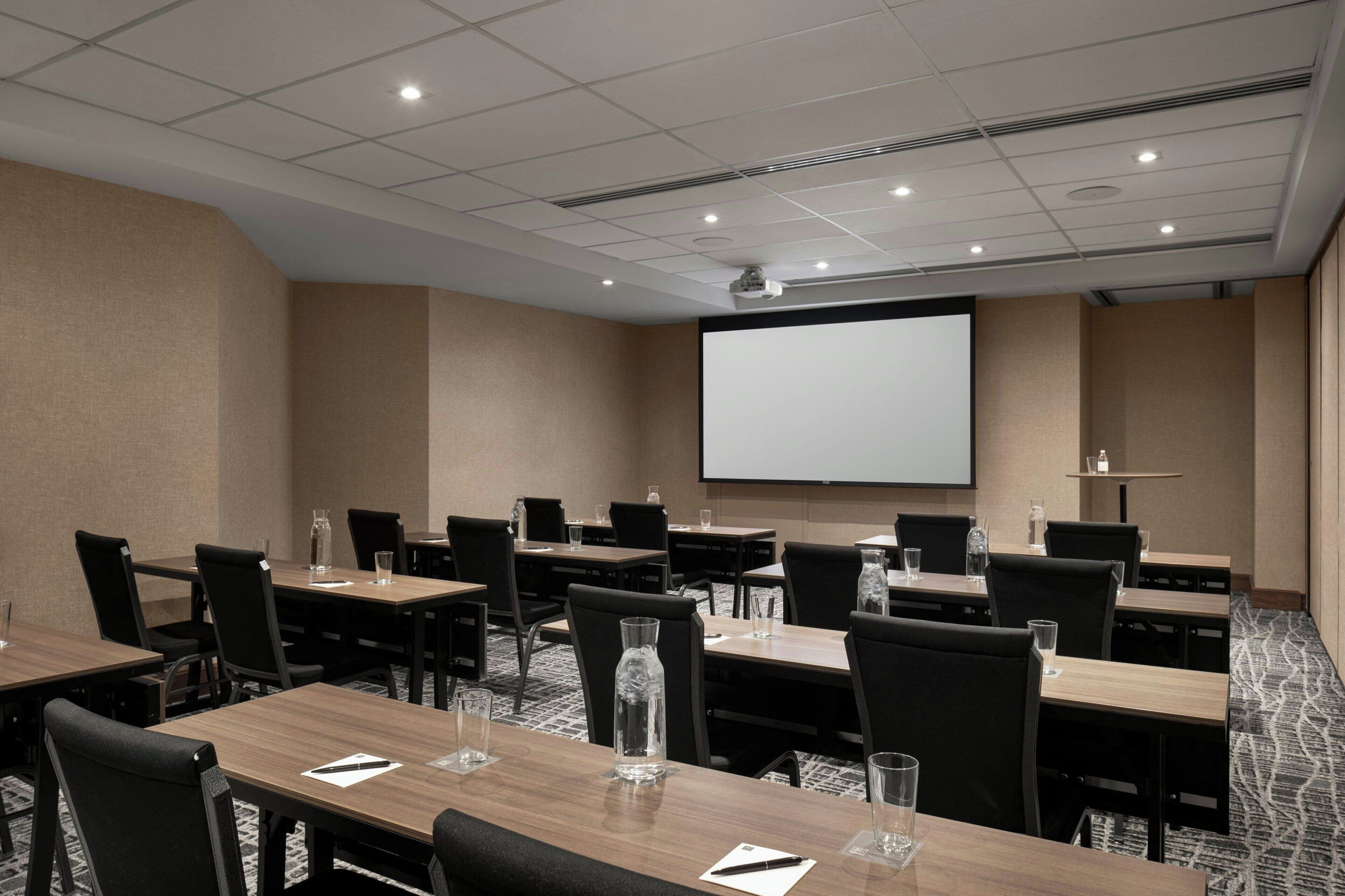 A conference room with multiple tables, chairs, a projector screen, and a carpeted floor.