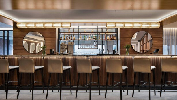 A modern bar area with wooden paneling, bar stools, and a well-lit counter with various bottles and glasses. - AC Hotel by Marriott Old Montreal (Montreal)