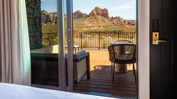 A balcony with a wooden deck, a wicker chair, and a view of red rock formations.
