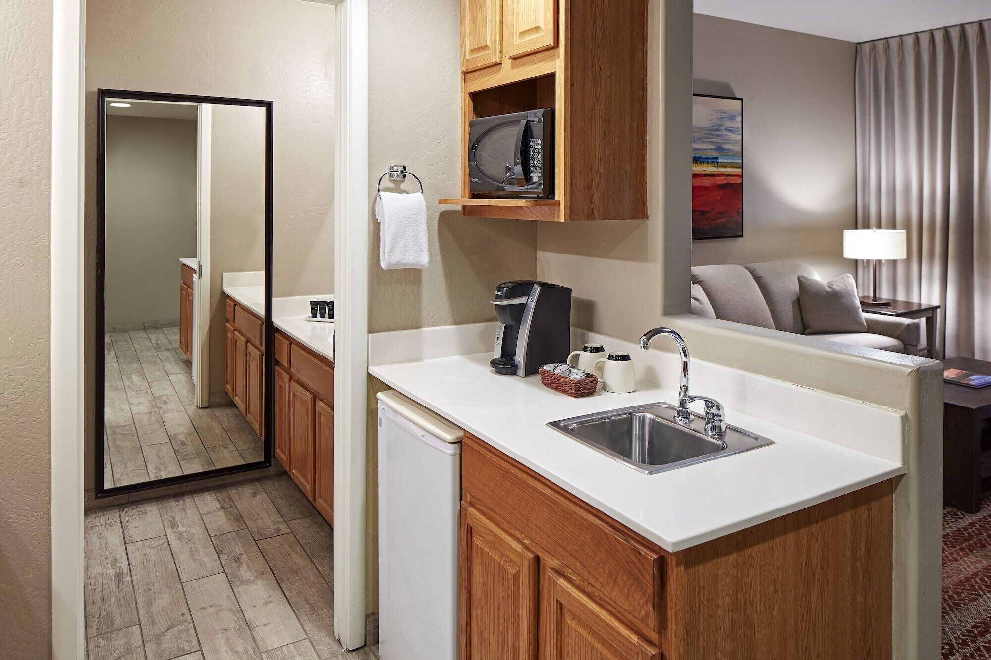 A compact hotel room with a kitchenette, a sink, a coffee maker, and a small cabinet.