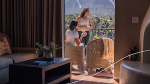 A room with a sofa, a coffee table, wicker chairs, and a view of mountains through a large window. - The Cliffs (Sedona)