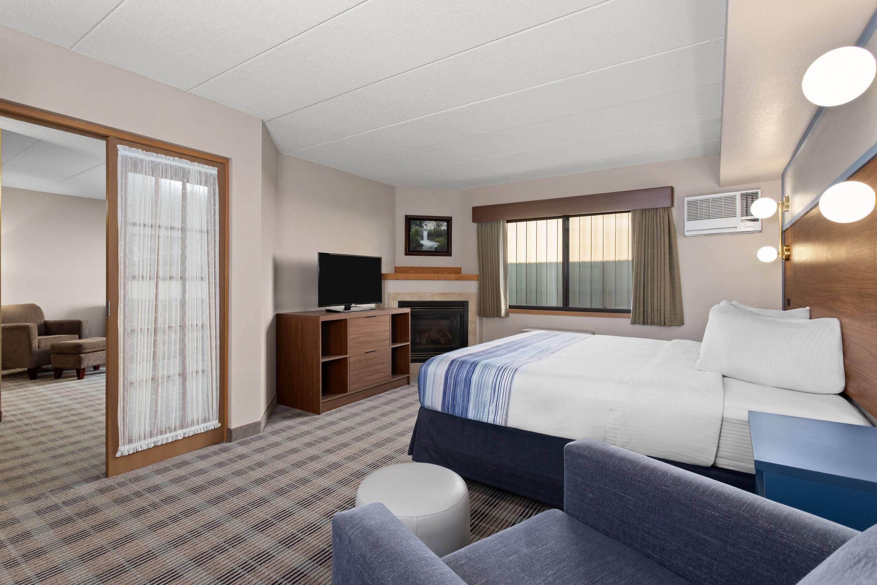 Habitación de hotel con cama, televisión, escritorio, silla, sofá, ventana y chimenea.