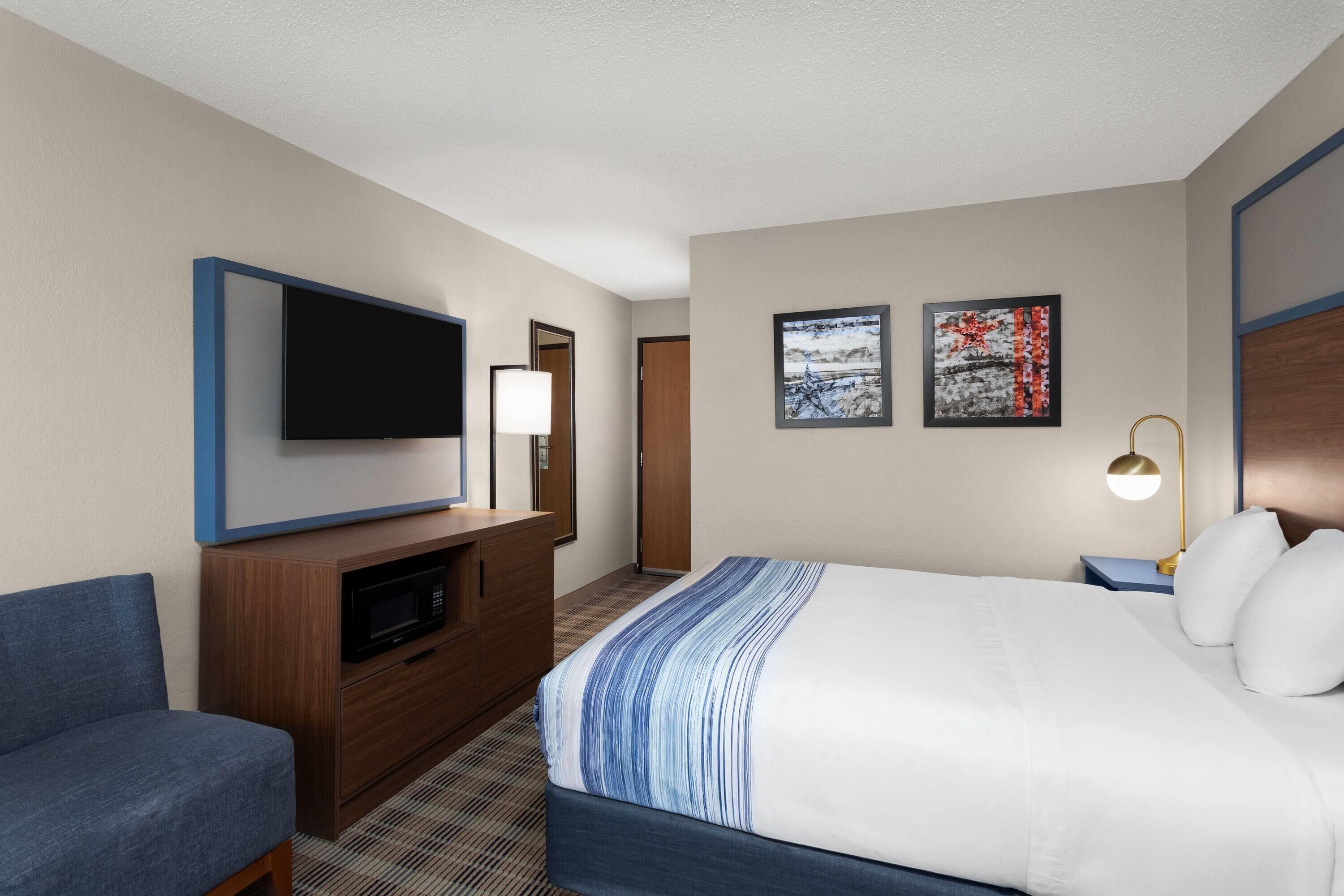 Habitación de hotel con cama, televisión, escritorio, silla y obras de arte en las paredes.