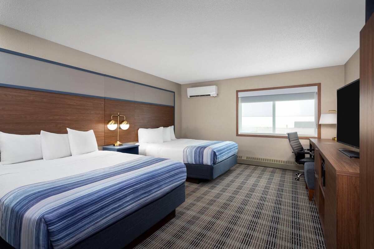 A hotel room with two beds, a desk with a computer, a TV, and a window with a view.
