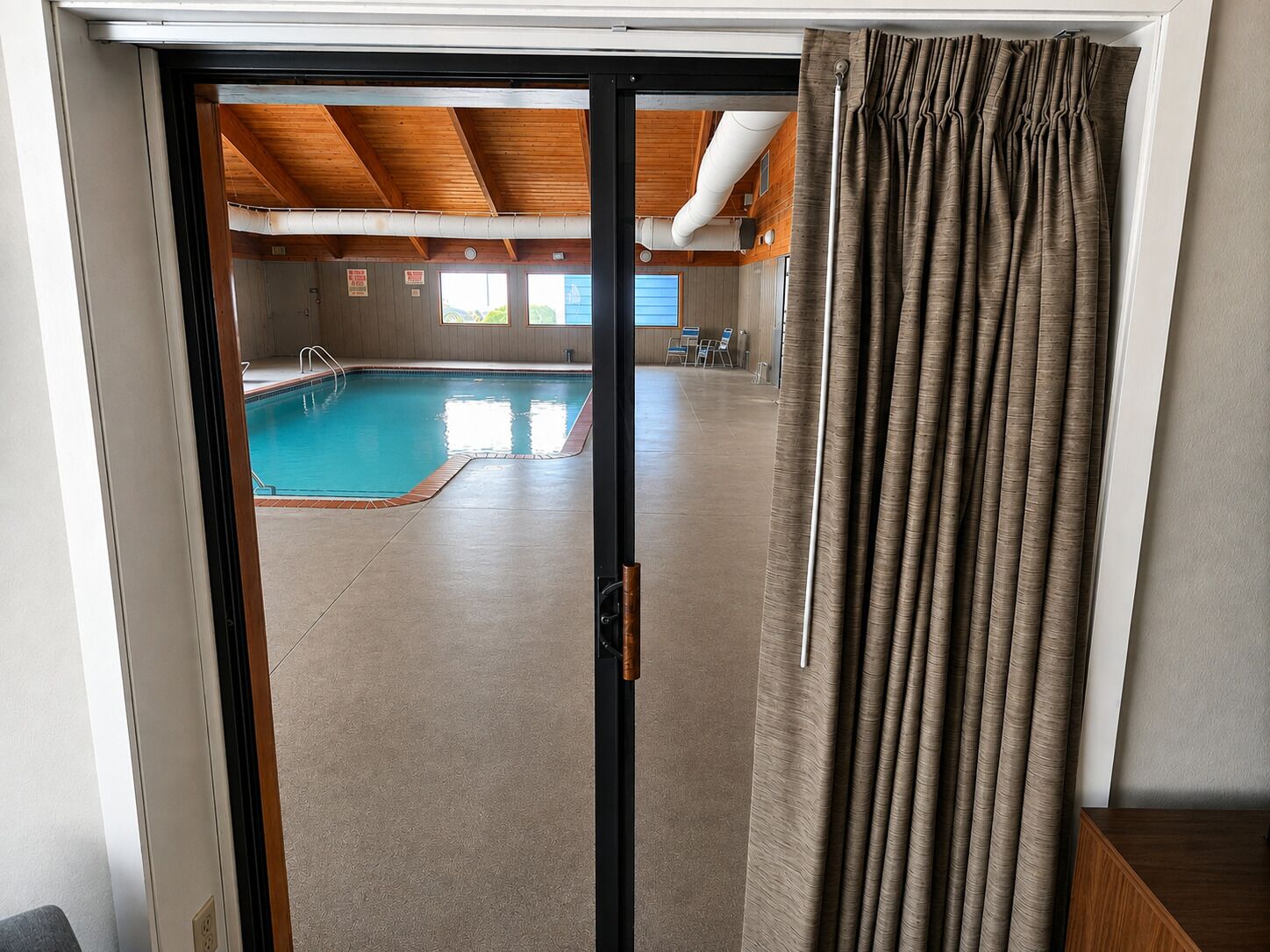 A view through a door into a swimming pool area with a wooden ceiling and a curtain.