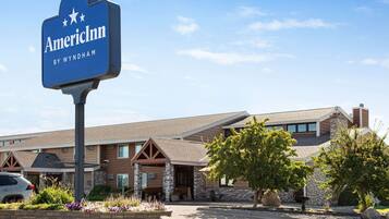 Een hotelschilt met 'AmericInn by Wyndham' en een gebouw met een gevel van natuursteen, meerdere ramen en een aangelegde voortuin.
