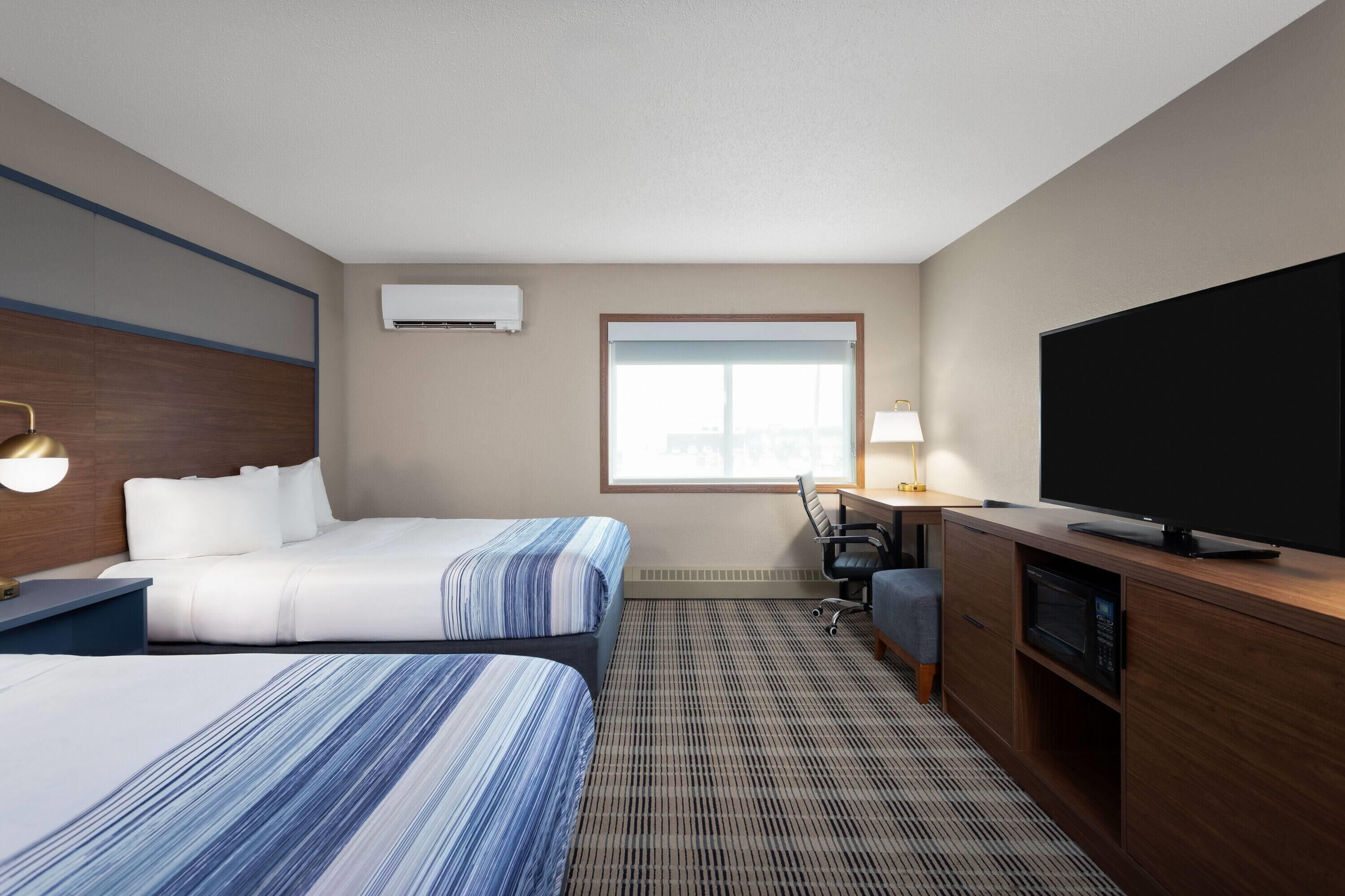 Ein Hotelzimmer mit zwei Betten, einem Schreibtisch, einem Fernseher und einer Klimaanlage.