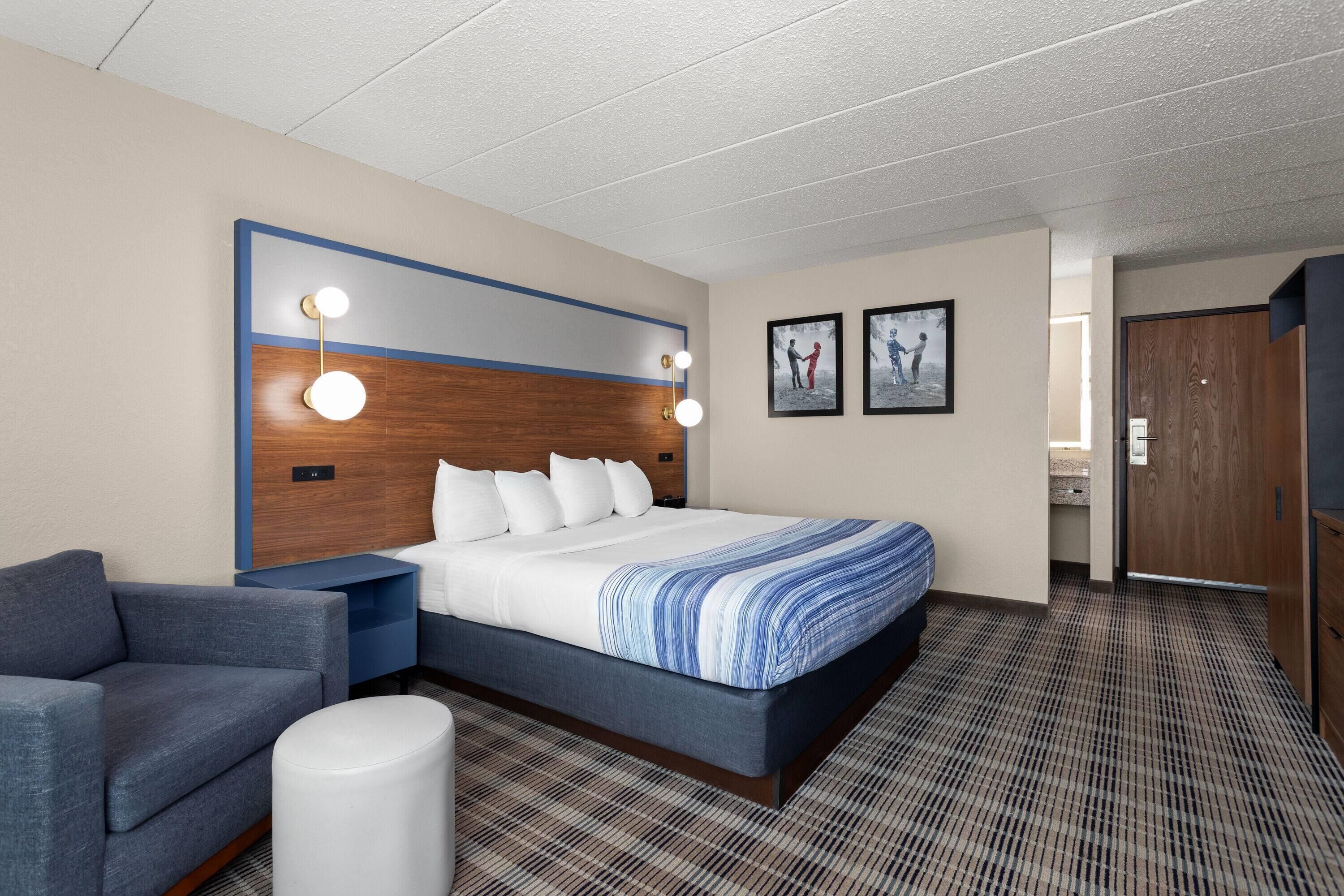 A hotel room with a large bed, a blue sofa, a small table, and a wall-mounted light fixture.