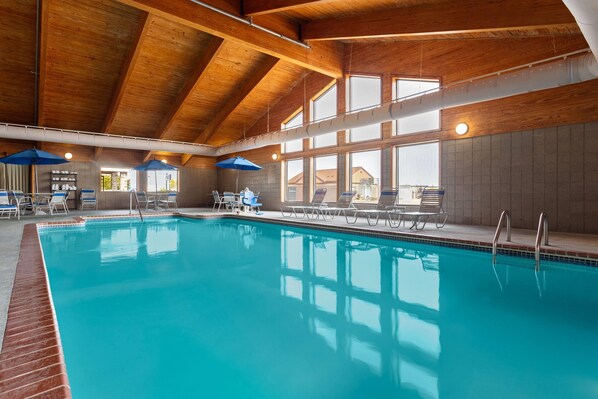 An indoor swimming pool with clear blue water, wooden ceiling beams, and sunlit windows. - AmericInn by Wyndham Roseau (Roseau)