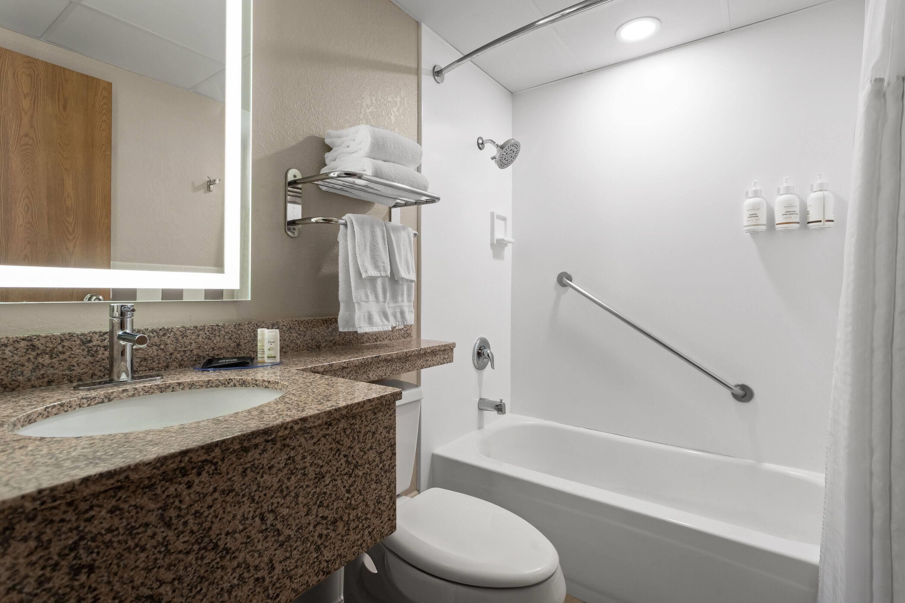 Un baño con lavamanos de encimera de granito, inodoro blanco, bañera blanca y ducha con cabezal de ducha de mano.