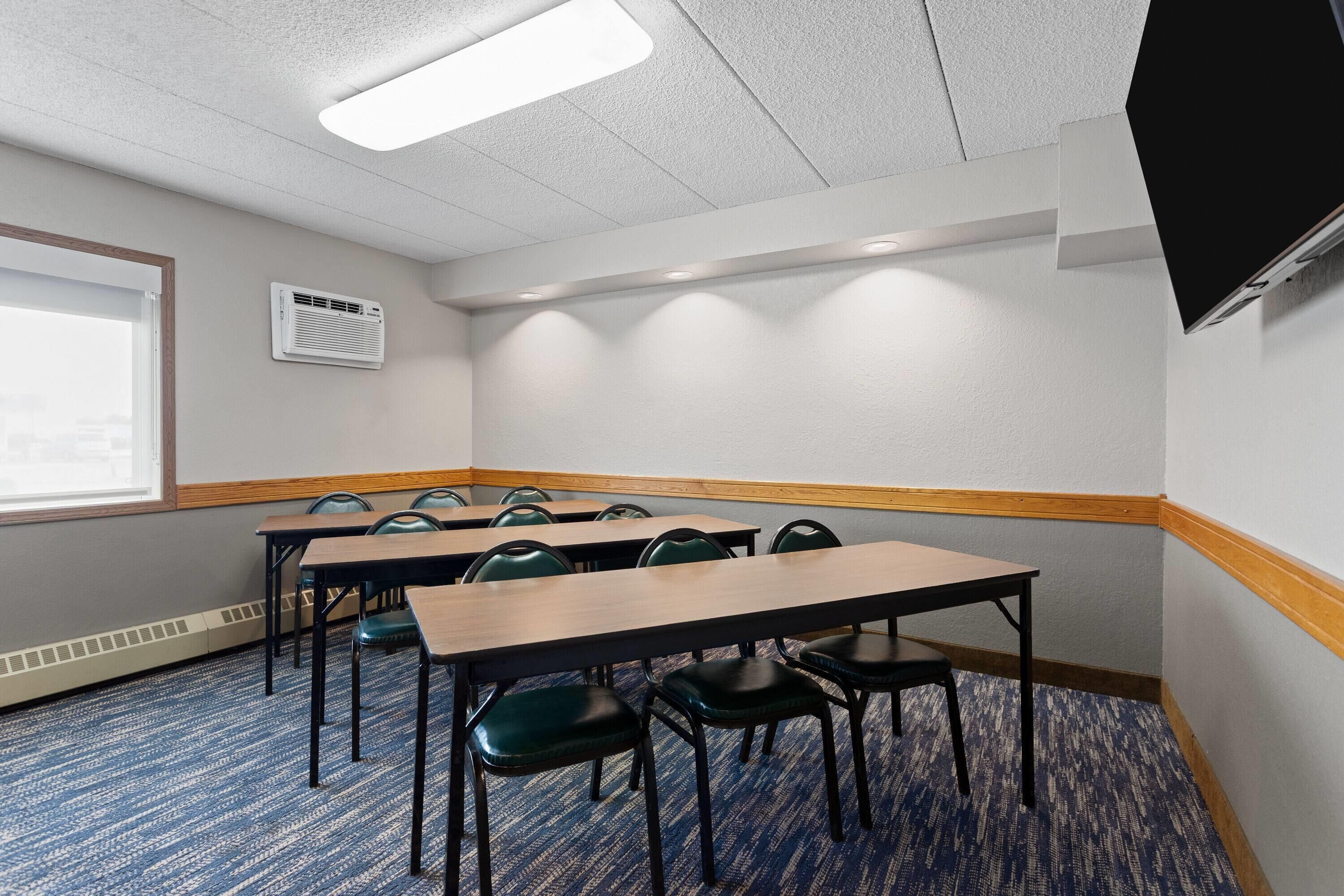 A conference room with tables and chairs, a projector screen, and a window.