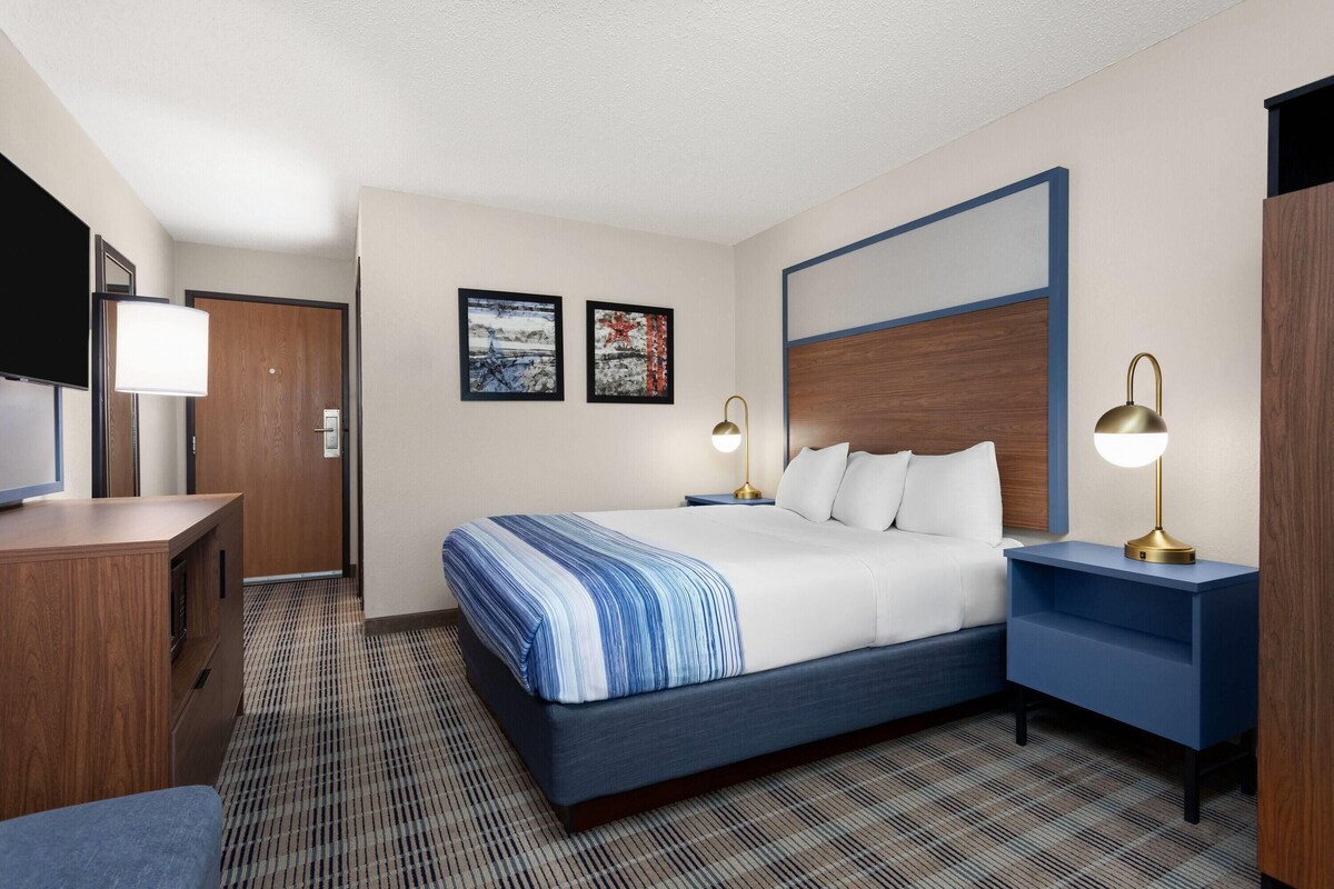A hotel room with a bed, bedside tables, a TV, and artwork on the wall.